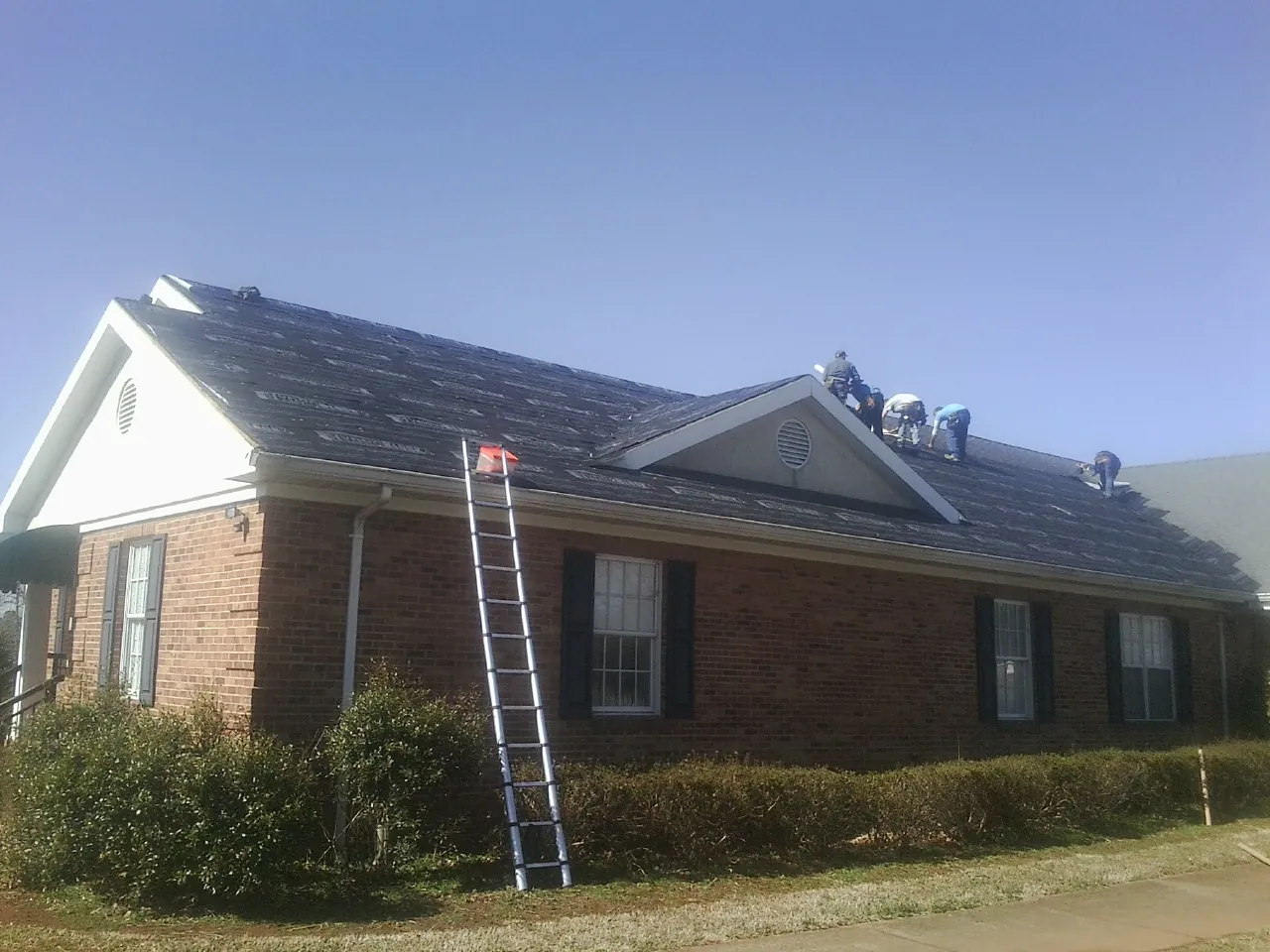 Crew tearing shingles off a brick ranch roof with a ladder set — Metal Roof Repair work by our crew in Kennedyville