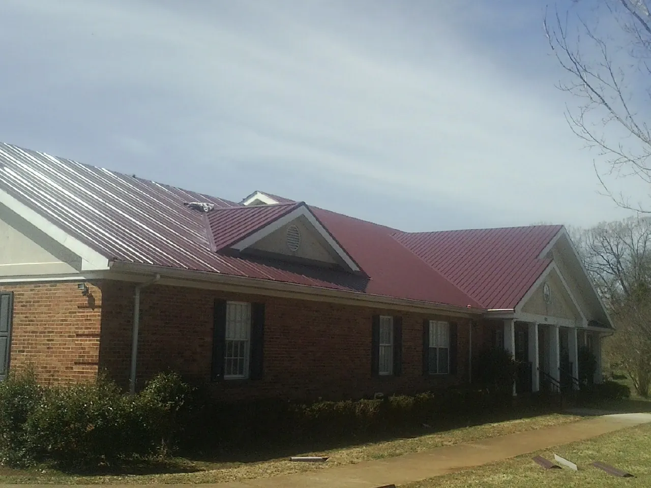 Red metal roof with gabled entries on a long brick building, from a Hail Damage Roof Repair job in Kennedyville
