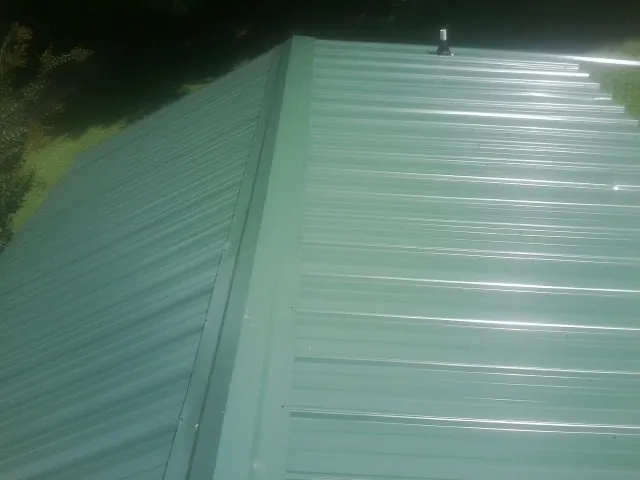 New green metal panels meeting at the ridge of a roof — Flat Roof Repair work by our crew in Kennedyville