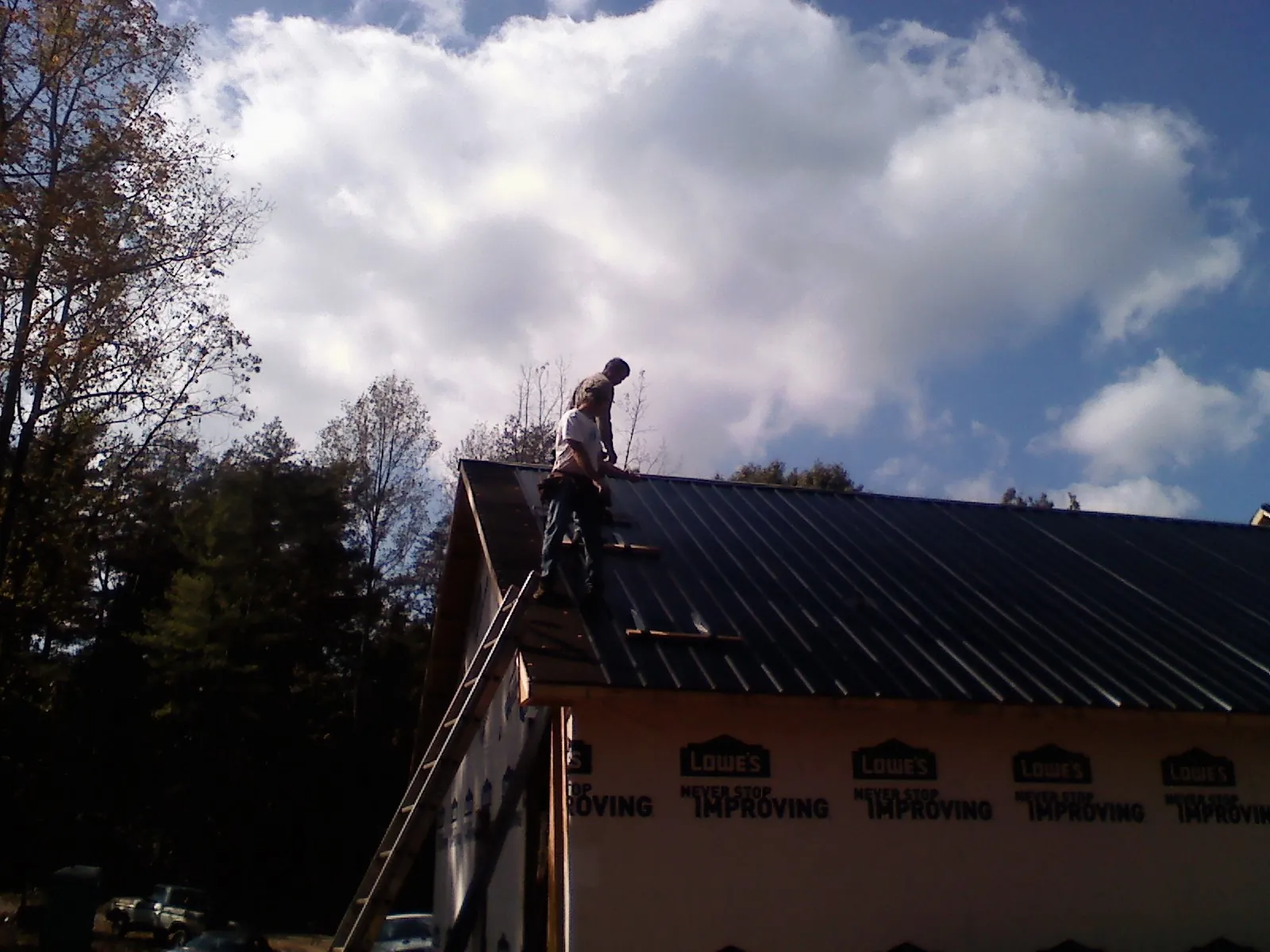 Roofer fastening dark metal panels high against a cloudy sky, from a Roof Inspection job in Kennedyville