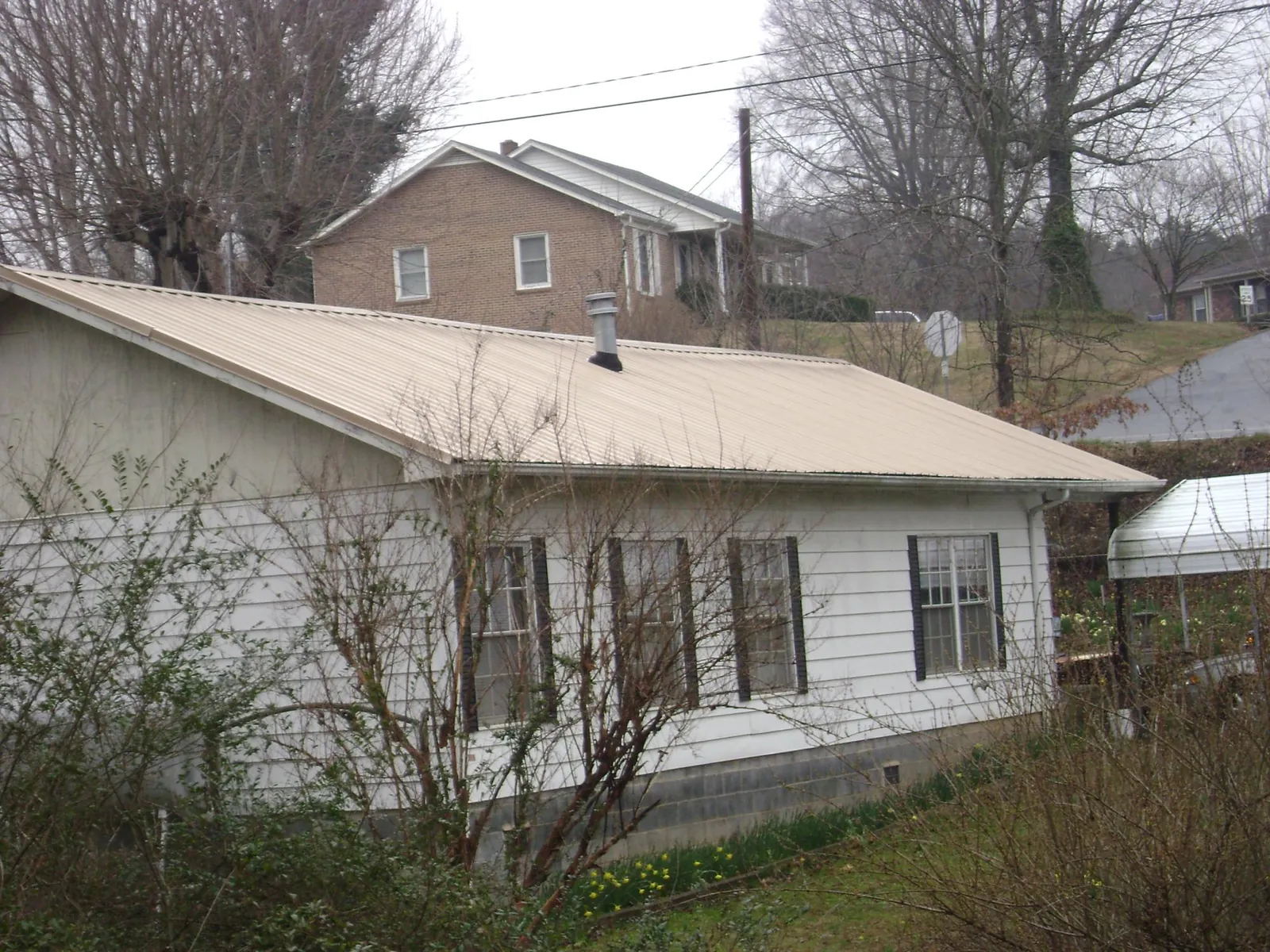 Tan metal roof on a white sided house set into a hillside — Commercial Roofing by Roofing Brothers in Kennedyville